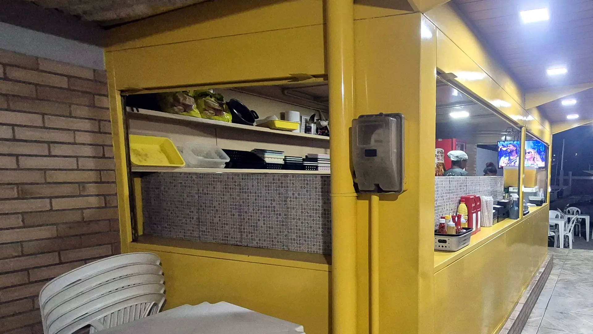 A Barraca do Baiano: balcão amarelo de onde saem os lanches e mesas brancas ao lado